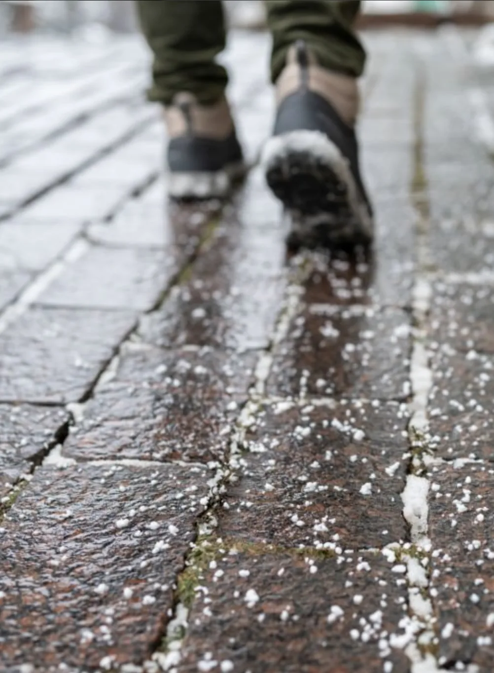 Icy walkway with pedestrian walking across snow and hail